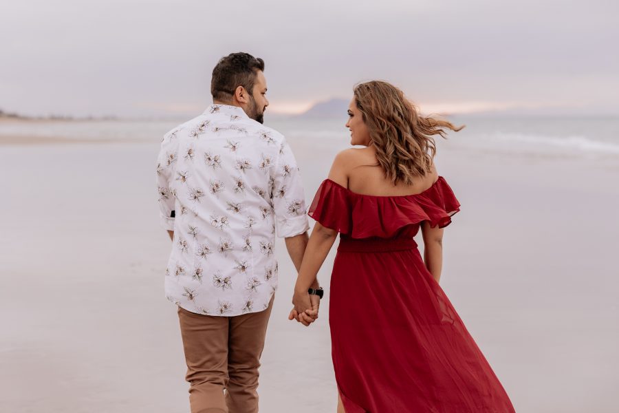 husband and wife walking away holding hands on beach during photo shoot