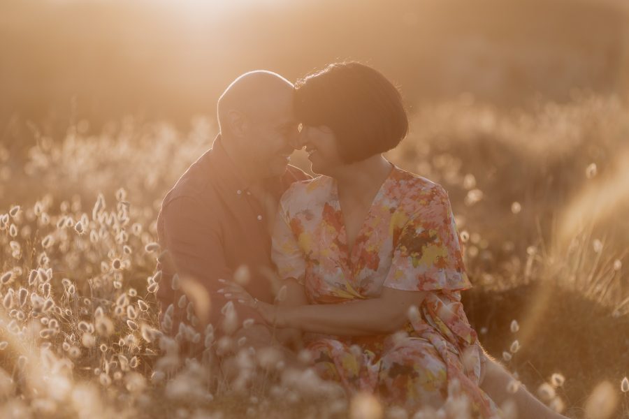 Engaged couple sitting in the sanddunes at golden hour with soft beach bunny tails around them