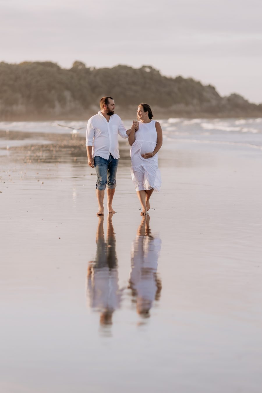 Maternity photo session walking in white dress with husband with water reflections Mount Maunganui