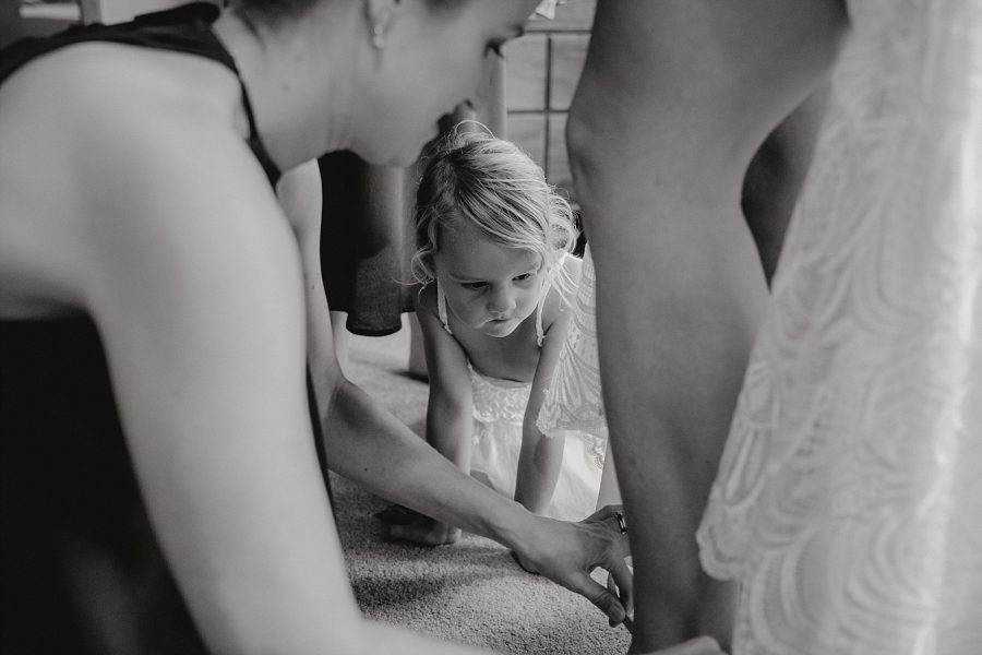 Young flower girl watching as bride puts on wedding shoes