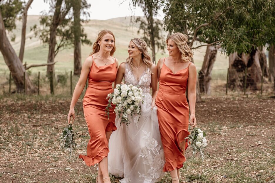 bride walks with happy bridesmaids in orange dresses