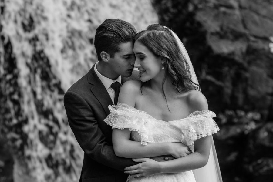 Black and white wedding photo of bridal couple's connection in front of waterfall