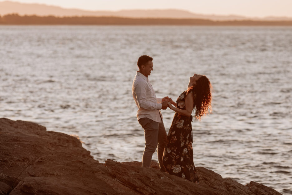 Candid happy laughing couple with sea behind them in Tauranga