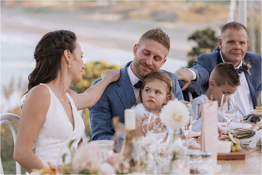 Bride and best man console groom at wedding table during speeches