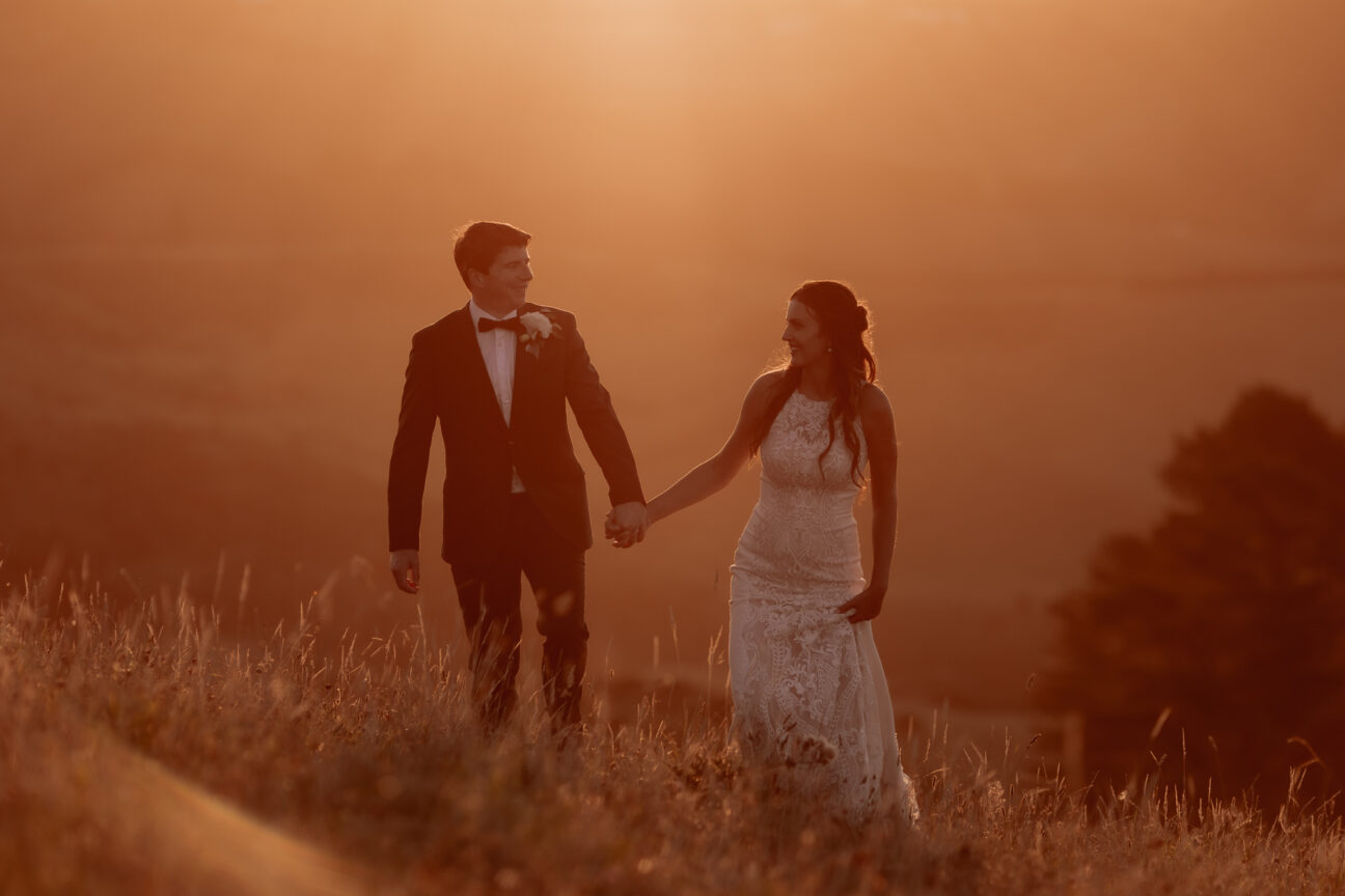 Beautiful image of bride and groom wedding photos with golden light behind them walking in the mountains in Tauranga New Zealand