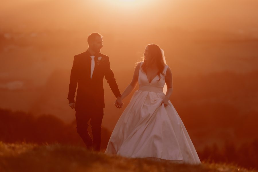 wedding couple holding hands walking up hill at sunset