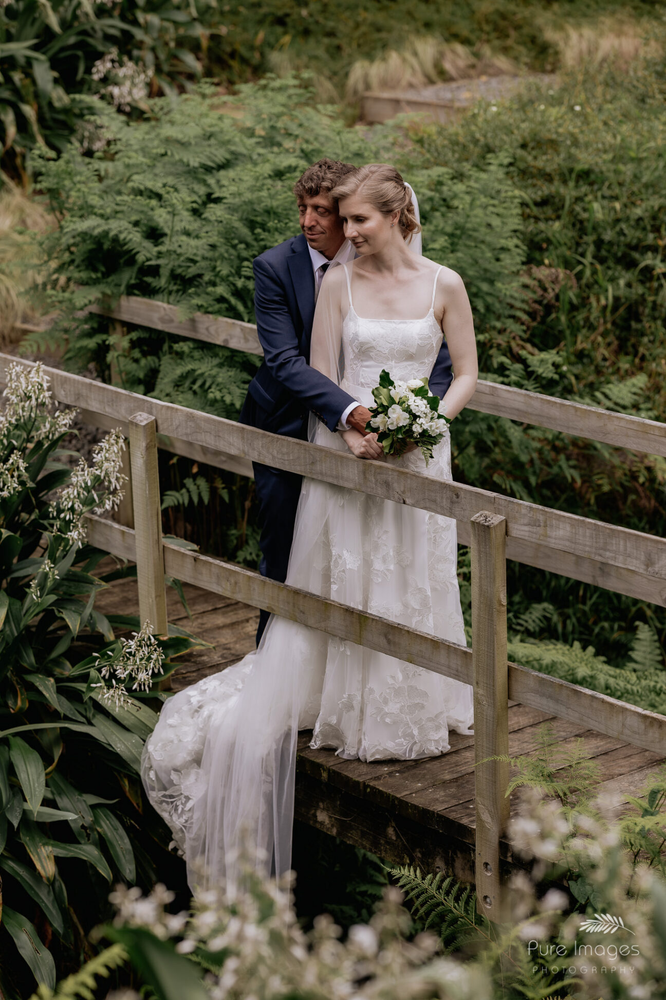 Bride and groom on bridge looking at stream