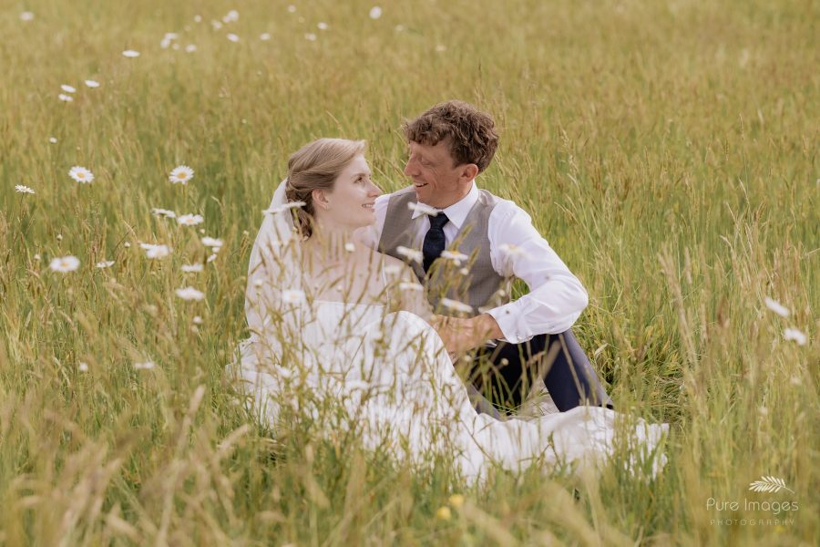 bride and groom sitting in field of daisies
