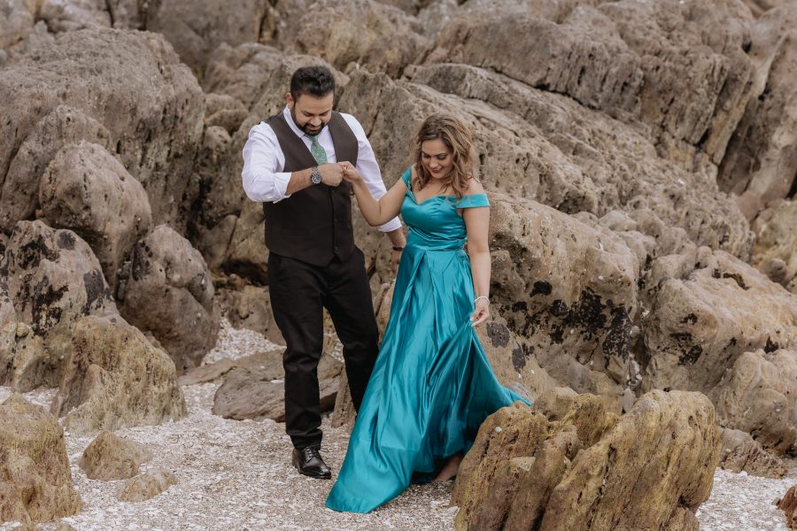 Couple in green dress walking through Rocks at Mount Maunganui beach