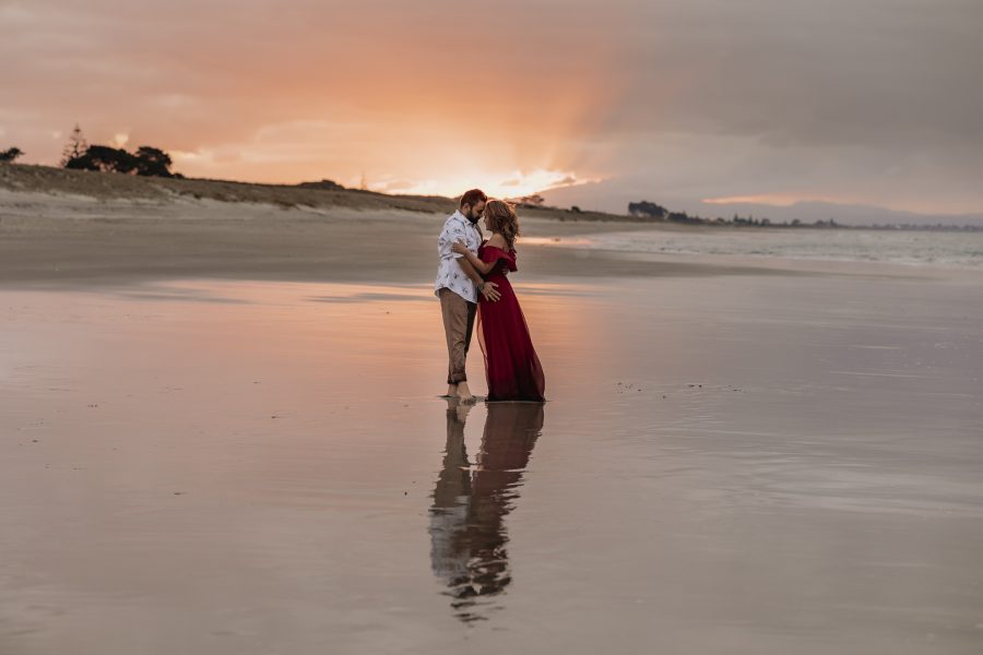 sun setting on papamoa beach during couple photos shoot lady in red dress