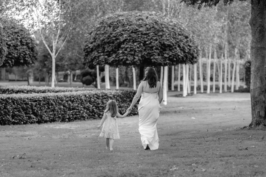 Bride walking away hand in hand with daughter in gardens at the tree church Ohaupo