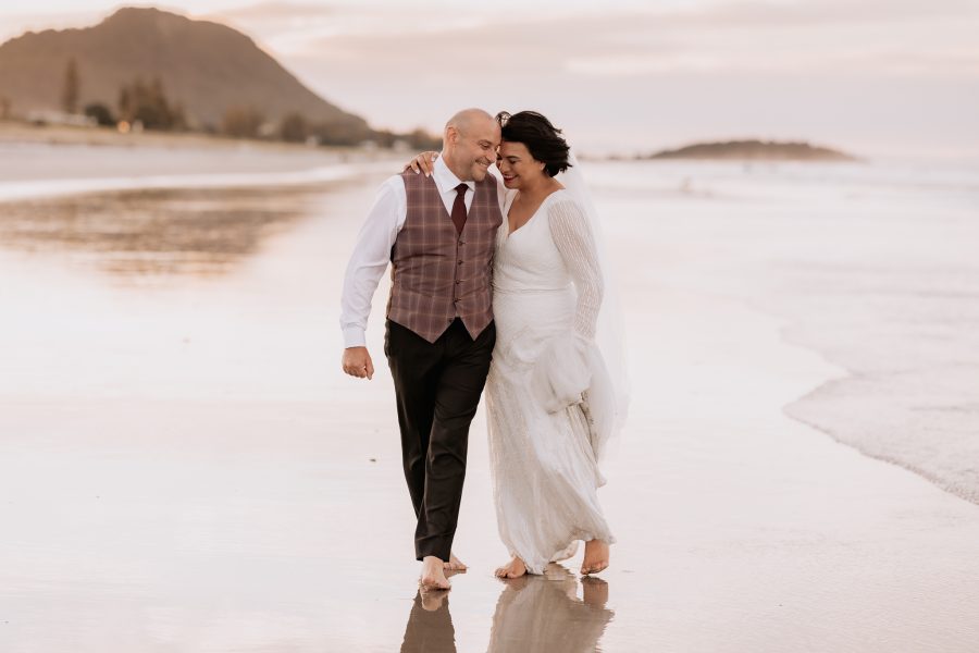 Wedding photos on Mount Maunganui beach walking laughing cuddling couple