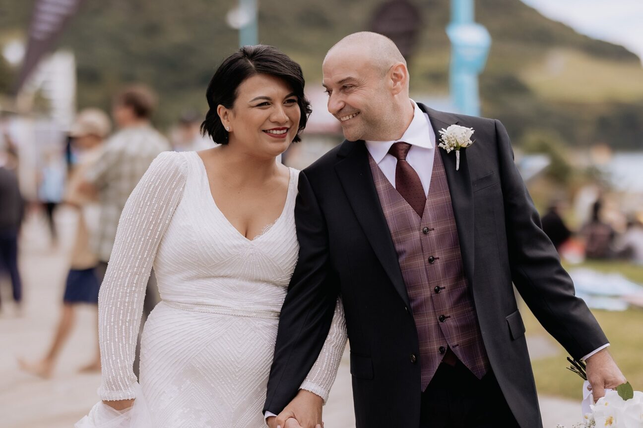 Laughing bride and groom on board walk at Mount Maungaui beach