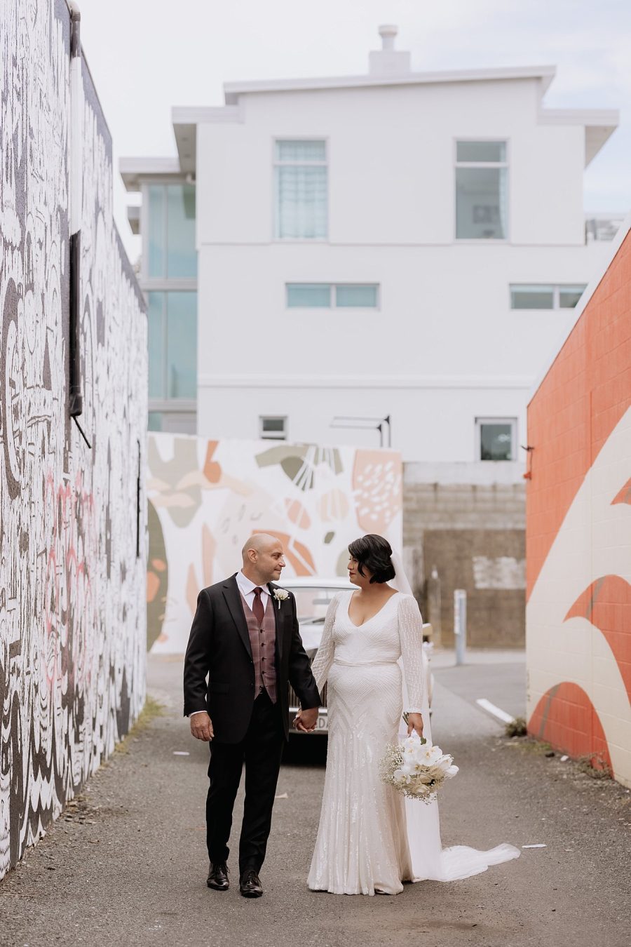 Wedding couple holding hands in front of deco mural with Rolls Royce behind them