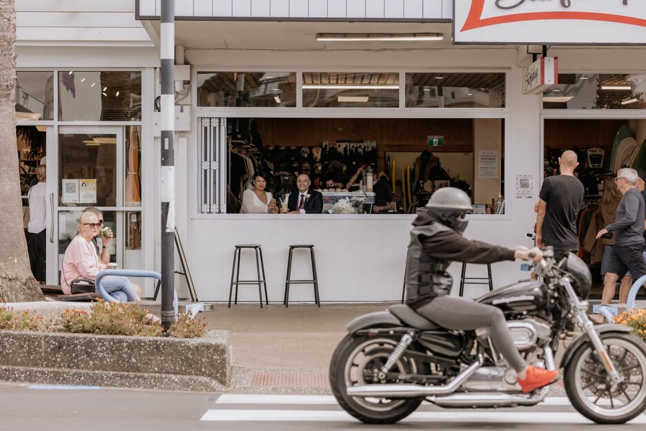 wedding couple having iced coffee Mount Surf shop window watching motorcycle drive by