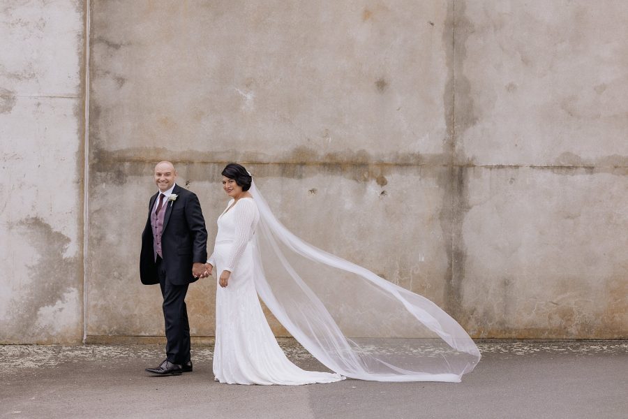 Bride and groom on own in front of concrete