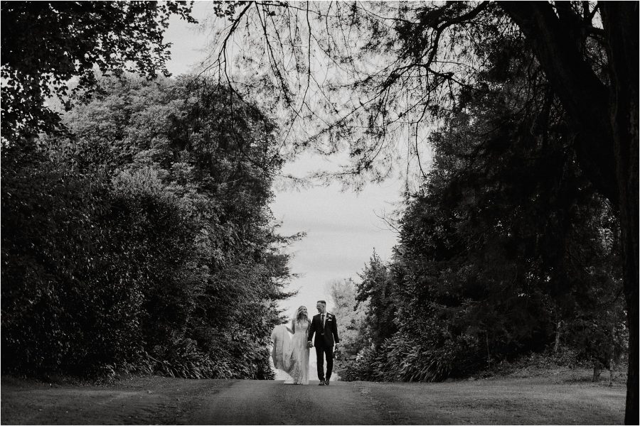 black and white image of bride and groom walking on driveway at kiwifruit orchard