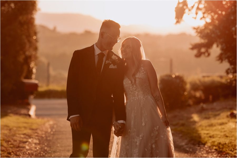 Bride cuddles groom walking at sunset