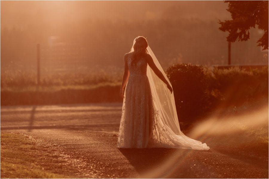 Bride holds out veil in golden light as sunshine shines through