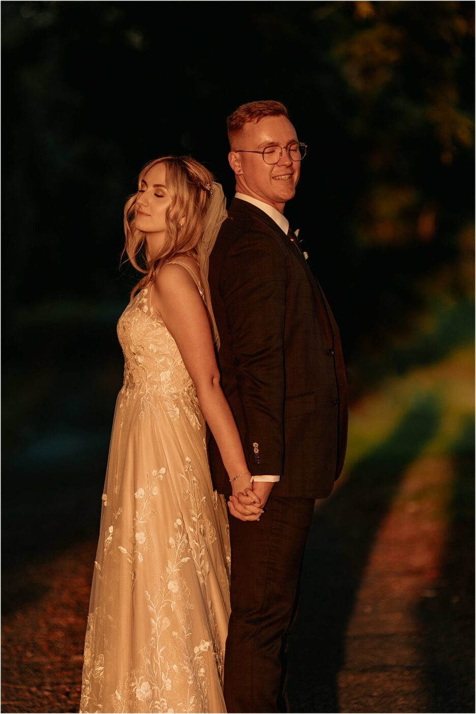 couple stand back to back as golden light hits their faces
