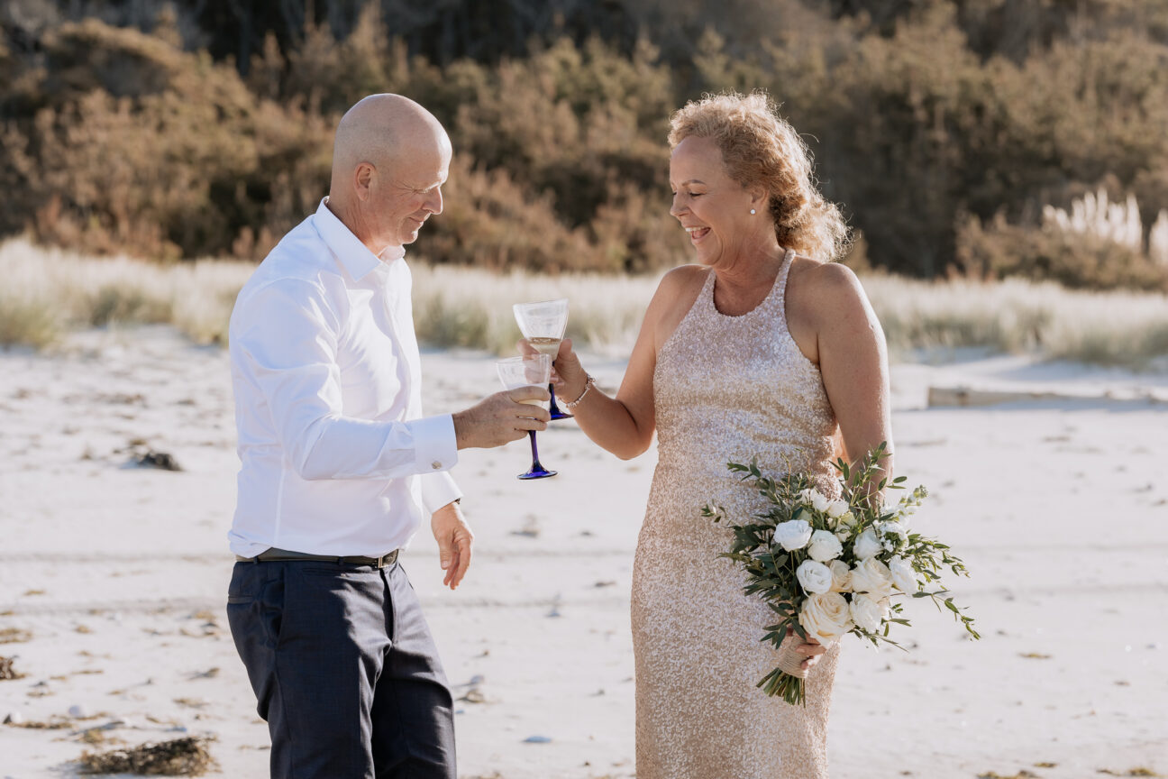 elopement couple celebrating with champagne glasses on beach