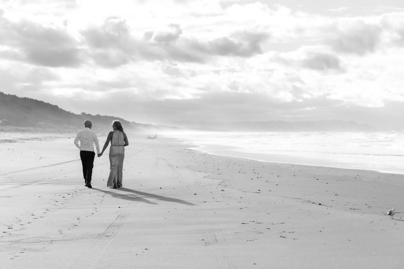 Bride and groom walking on beach hand in hand on Matakana Island