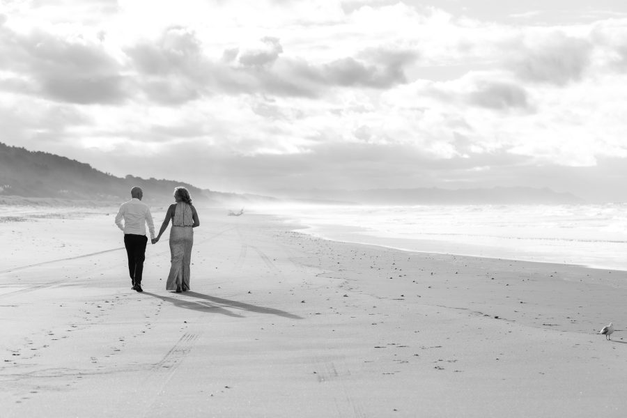 Bride and groom walking on beach hand in hand on Matakana Island