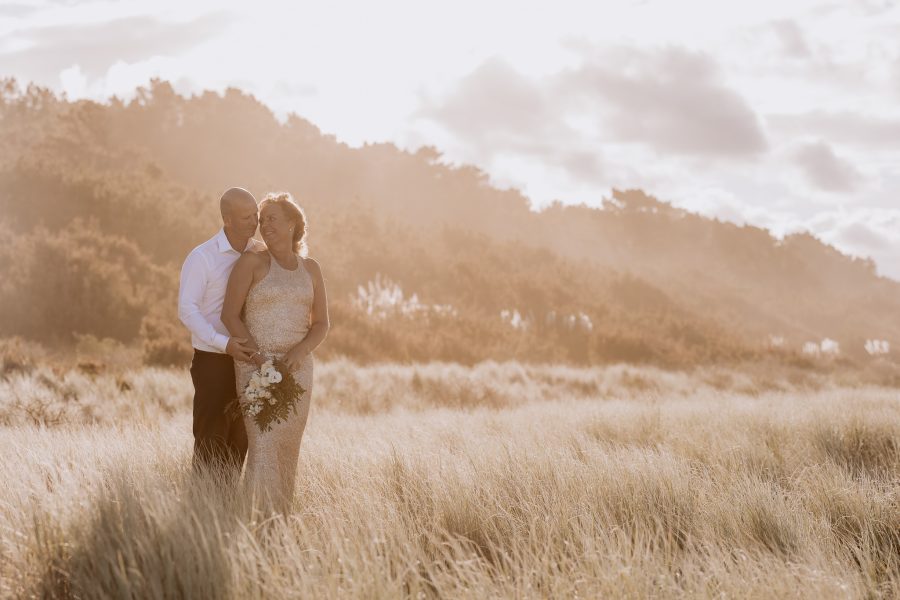 Wedding couple in sand dunes on Matakana Island in golden sunlight