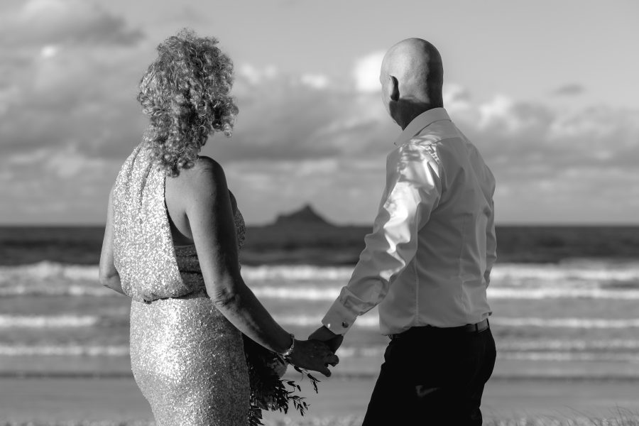 Elopement couple holding hands looking at the island on Matakana beach wedding