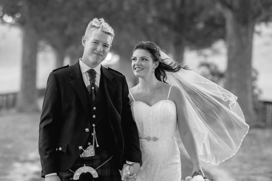 Bride looks at groom smiling, groom in kilt looks at camera