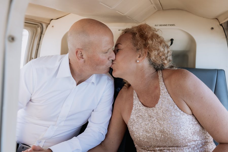 Groom kissing bride in back of helicopter in sky above Tauranga