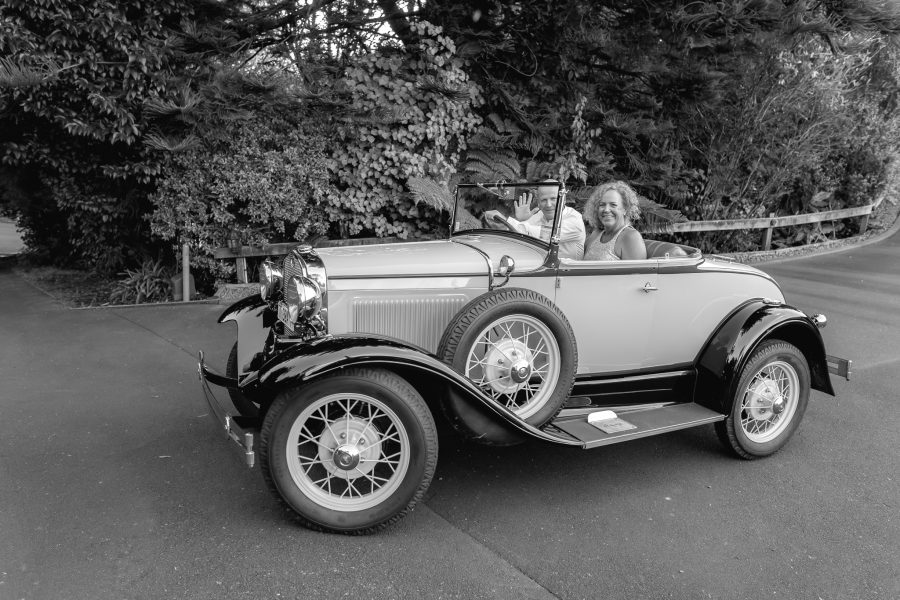 Bride and groom waving while driving his vintage car