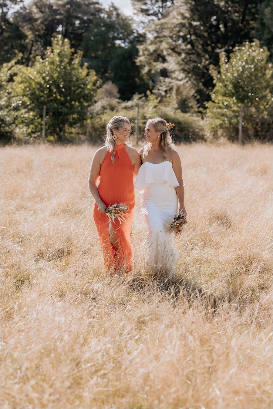 Bride with sister in orange bridesmaids dress walking in summer field