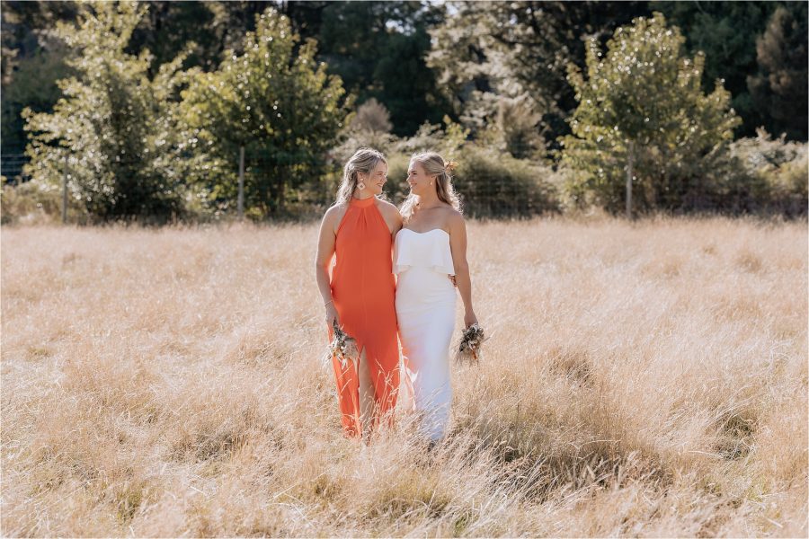 Natural photos of bride hanging out with bridesmaid walking in high dry grass fields in Ohakune backyard wedding