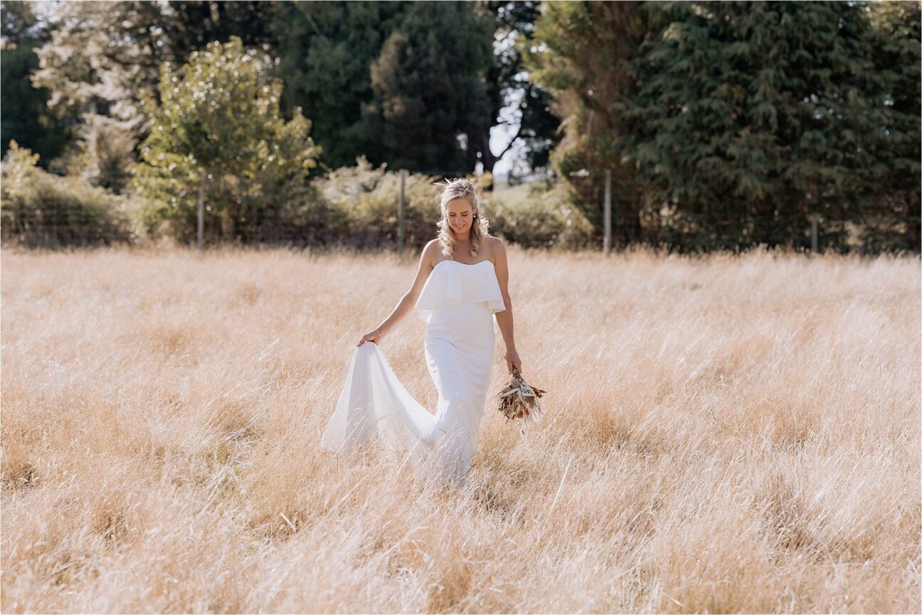 Bride walking in fields of high grass in Summertime in Manawatu back yard wedding