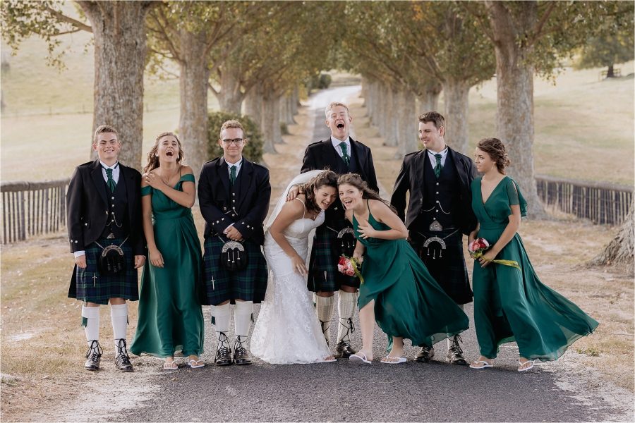 wedding party having alot of fun being silly on red barn driveway