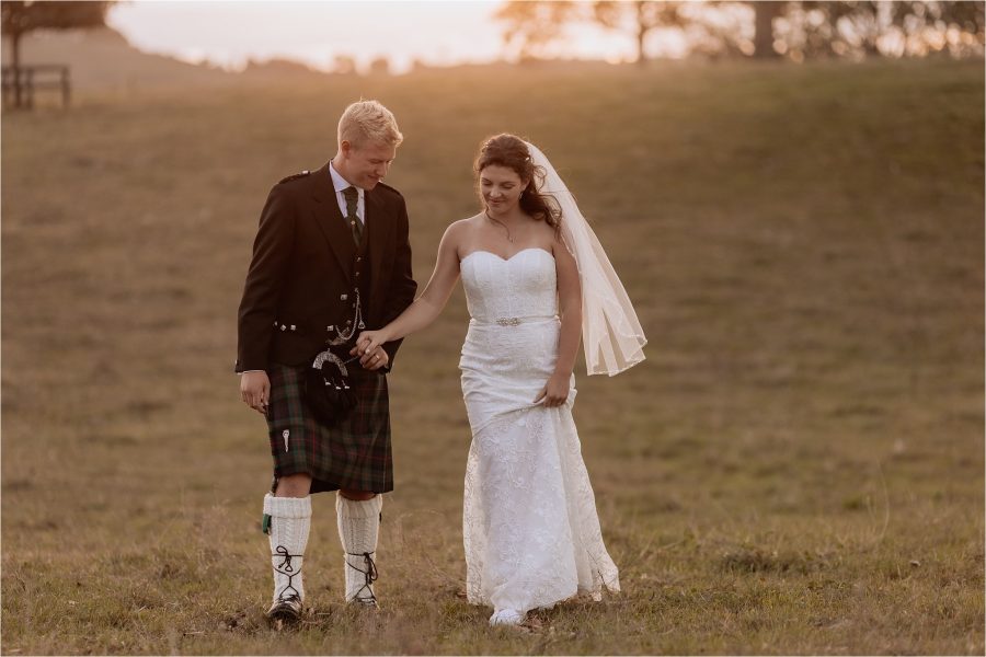 Bride and groom walking along paddock in their own time at red barn