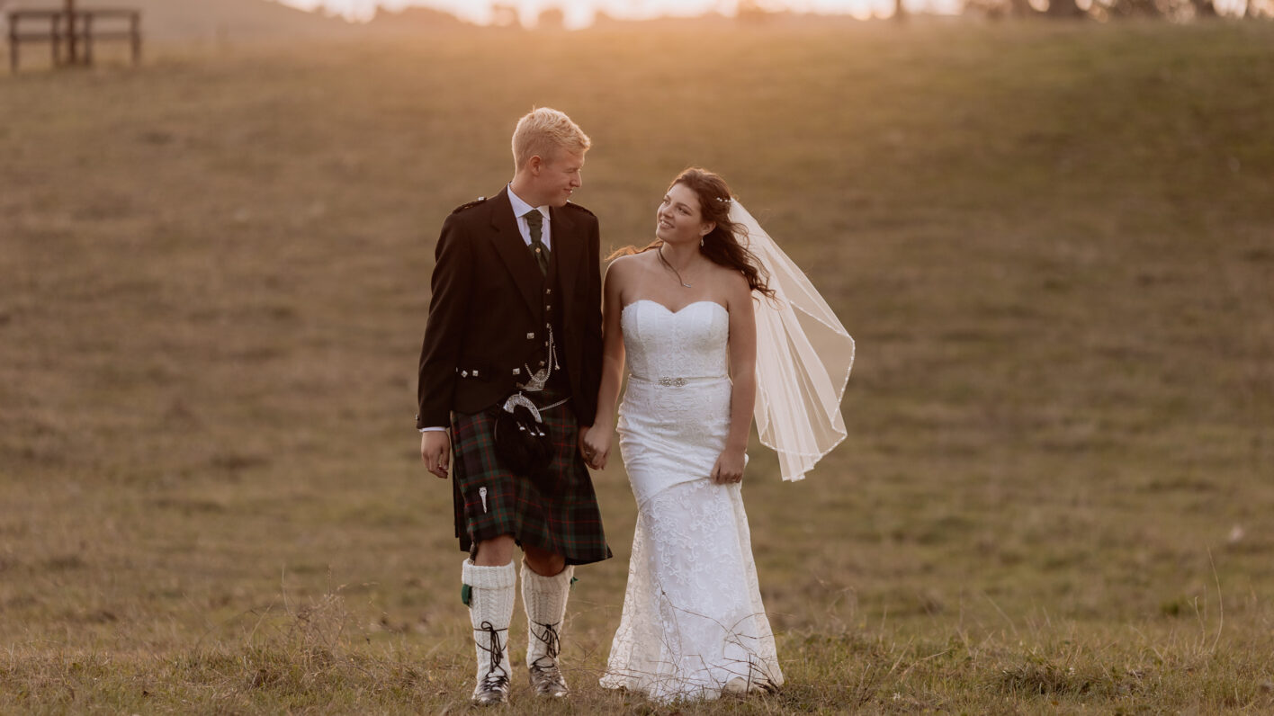 Bridal couple walking on field at Red Barn Venue New Zealand in the golden sunset