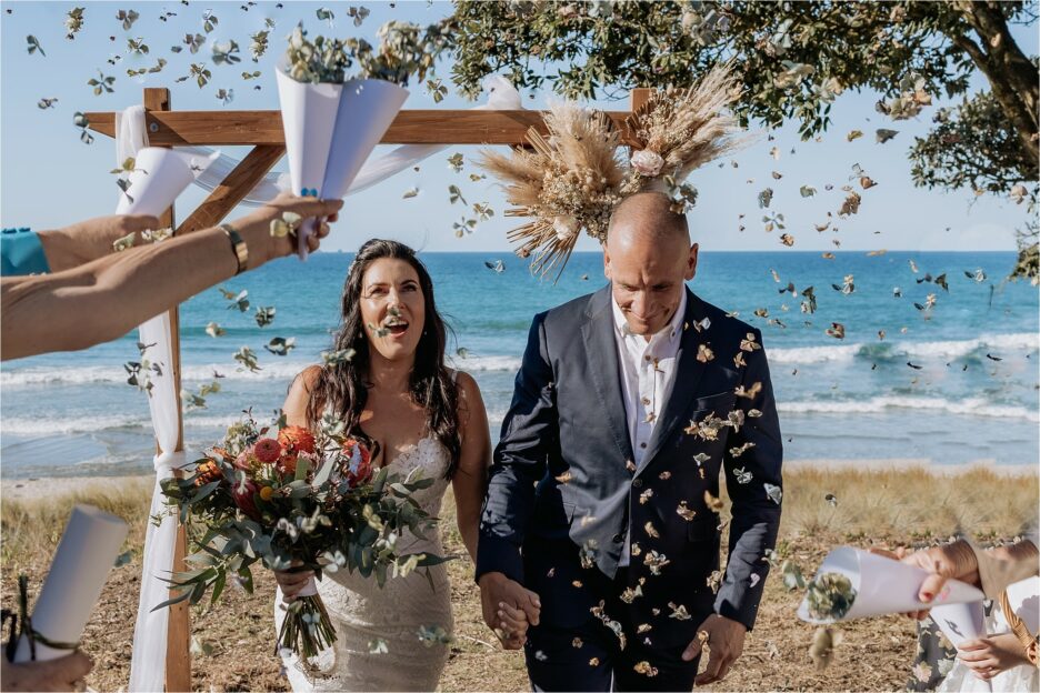 Guests throw confetti and bride and groom walk up aisle laughing