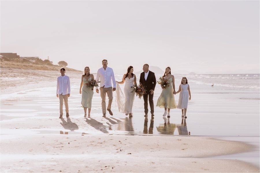 Wedding party walking on beach with Mount Maunganui in background