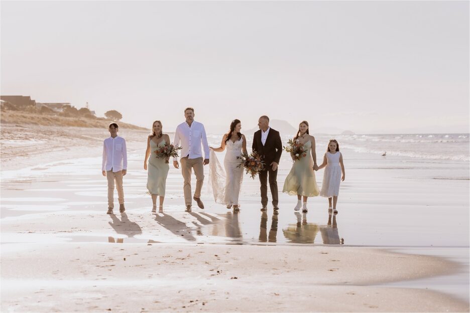 Wedding party walking on beach with Mount Maunganui in background