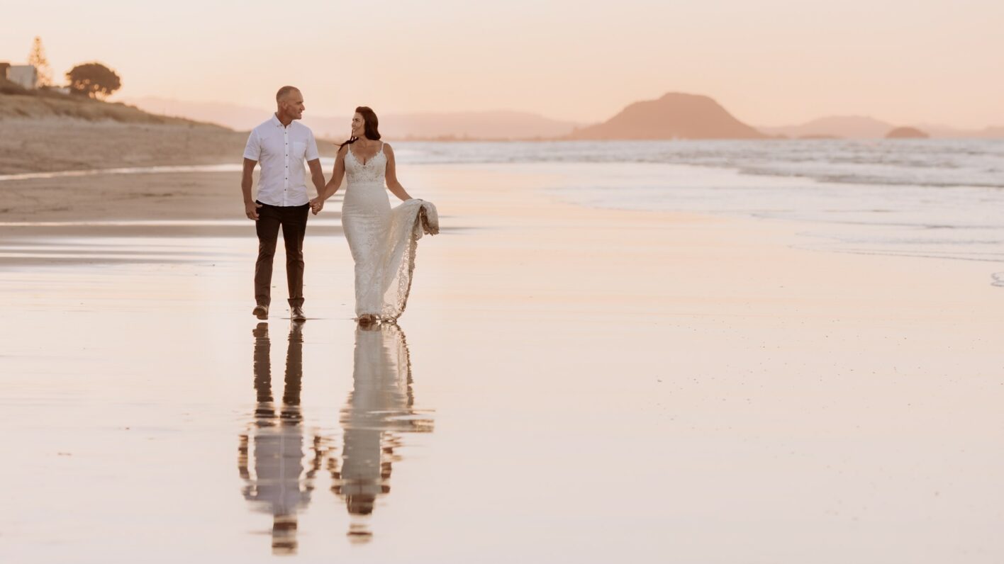 bride and groom walking at golden hour on beach with reflections