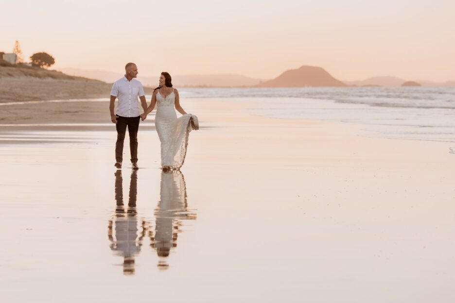 bride and groom walking at golden hour on beach with reflections