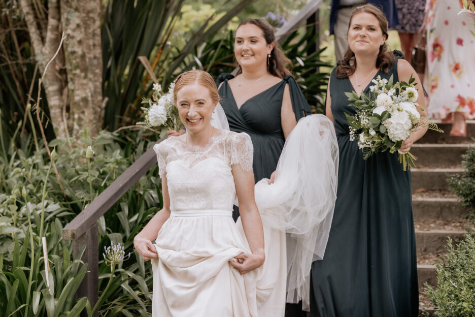 Bride walking down stairs with bridesmaids in green dresses before wedding ceremony at Old Forest School