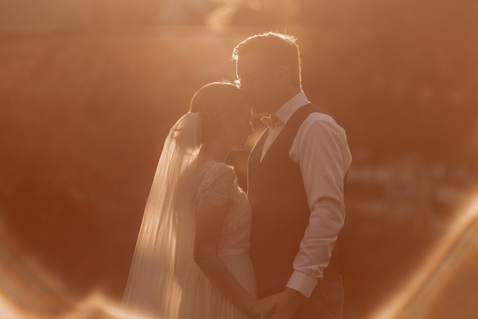 Groom kisses bride on head in golden light at Old Forest School