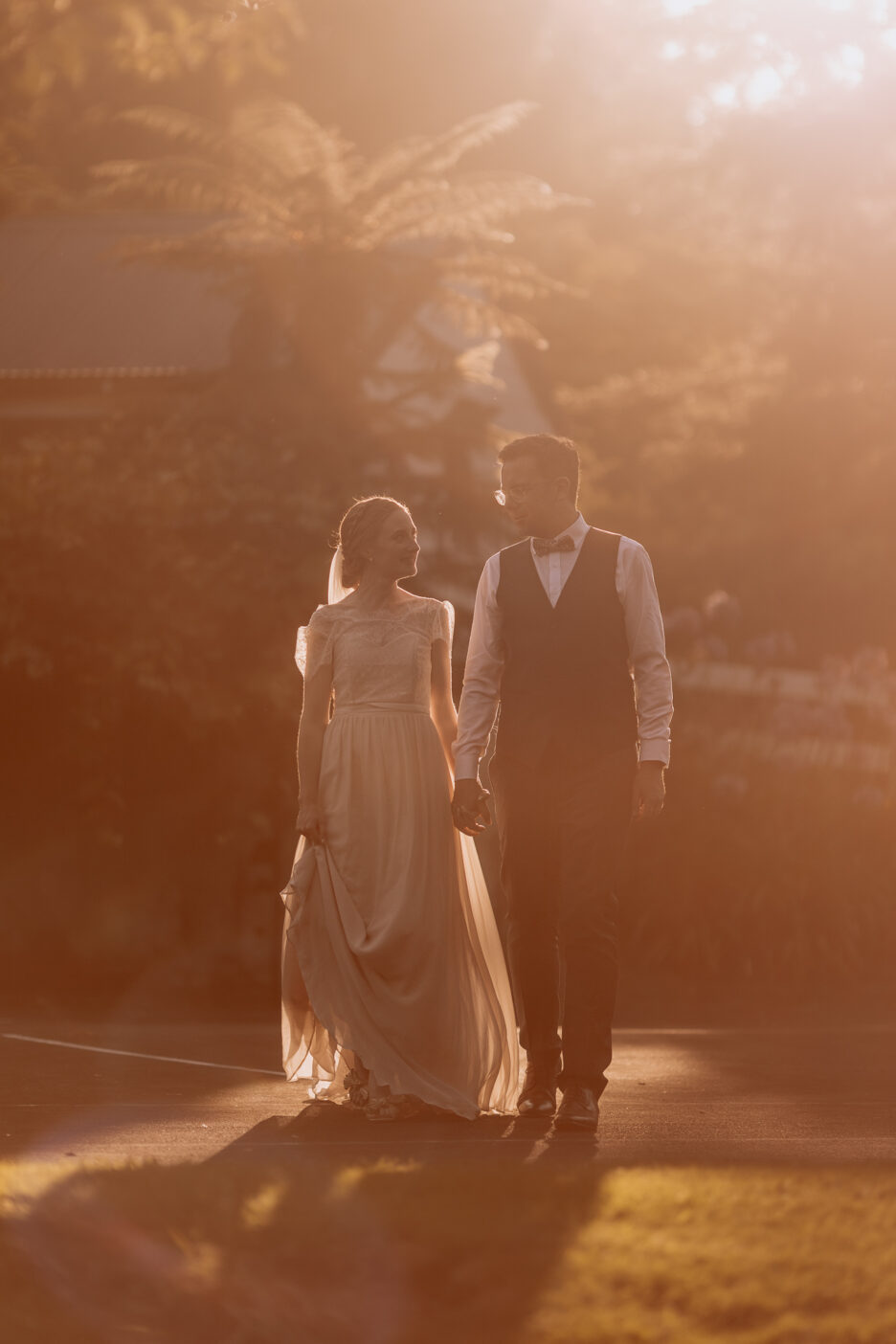 Golden light streams around bride and groom walking during golden hour
