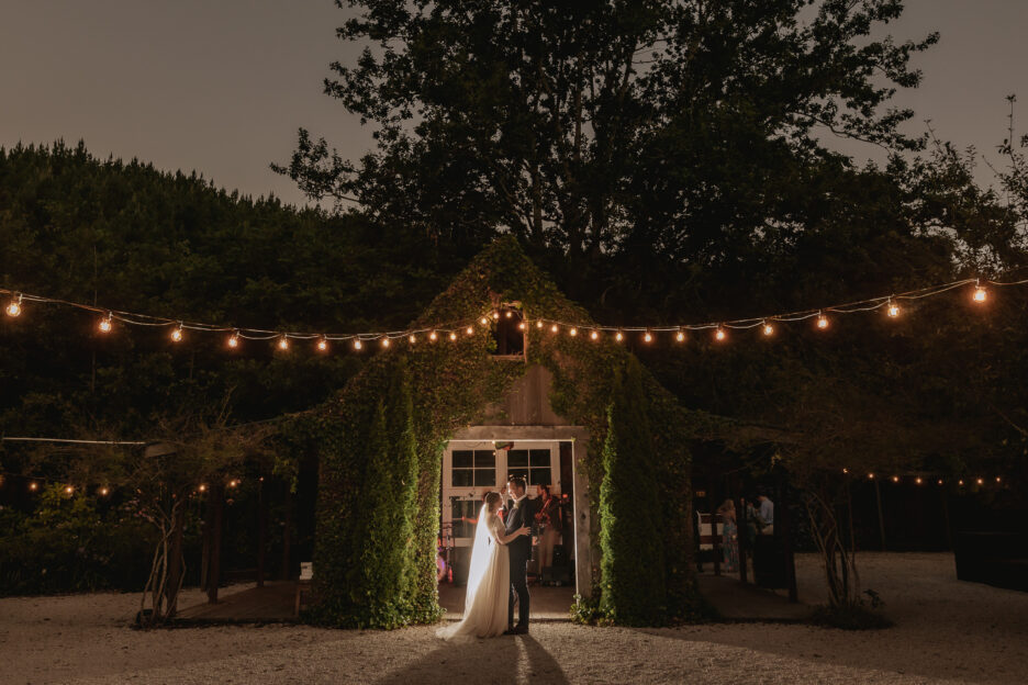 Night image of wedding couple dancing first dance outside Old Forest School redwood barn