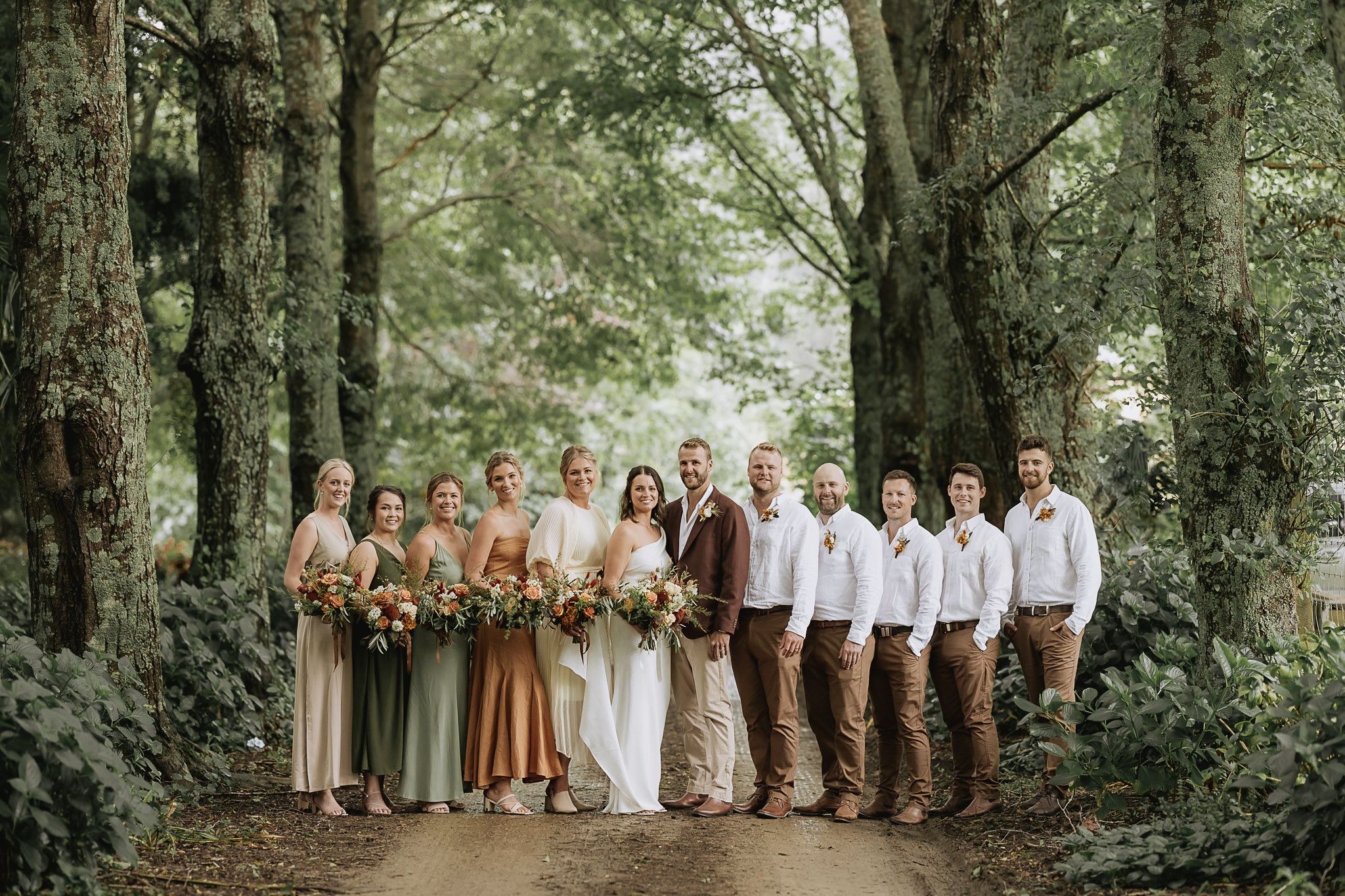 Country wedding party photo in rustic colours in beautiful driveway of The Run Whakatane