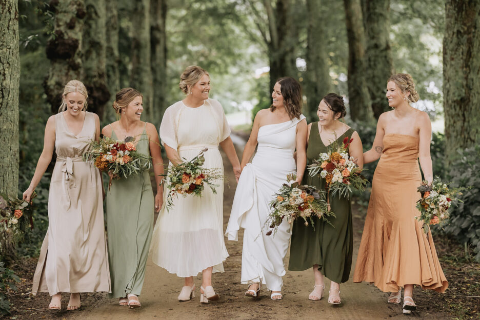 Mixed bridesmaids in autumn coloured dresses walking in county driveway New Zealand