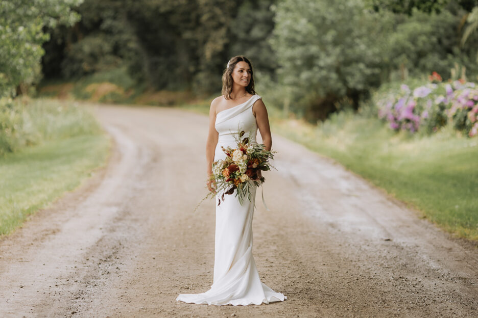 Bride in bridal studio dress on country road with rustic autumn toned bouquet